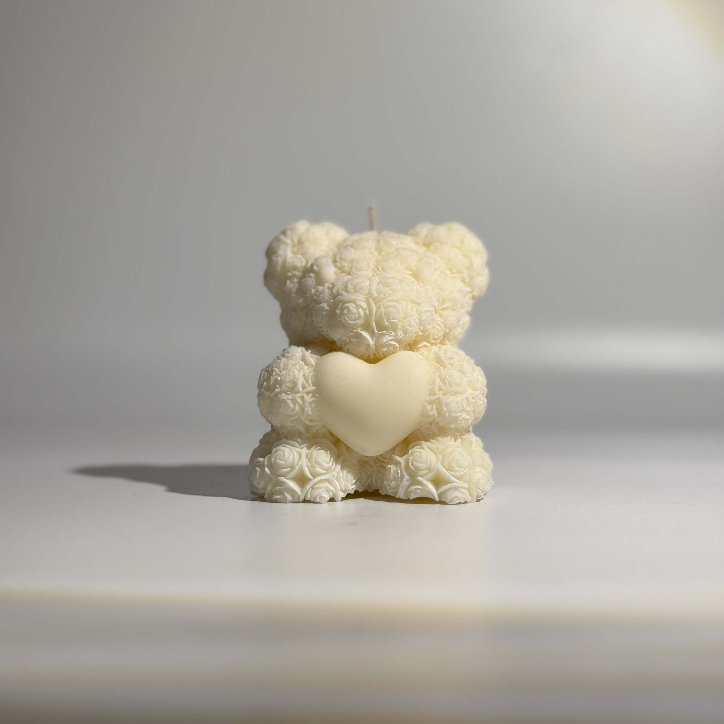 Ourson en rose en cire, décoré de roses délicates, tenant un cœur, symbole d'amour et de tendresse.